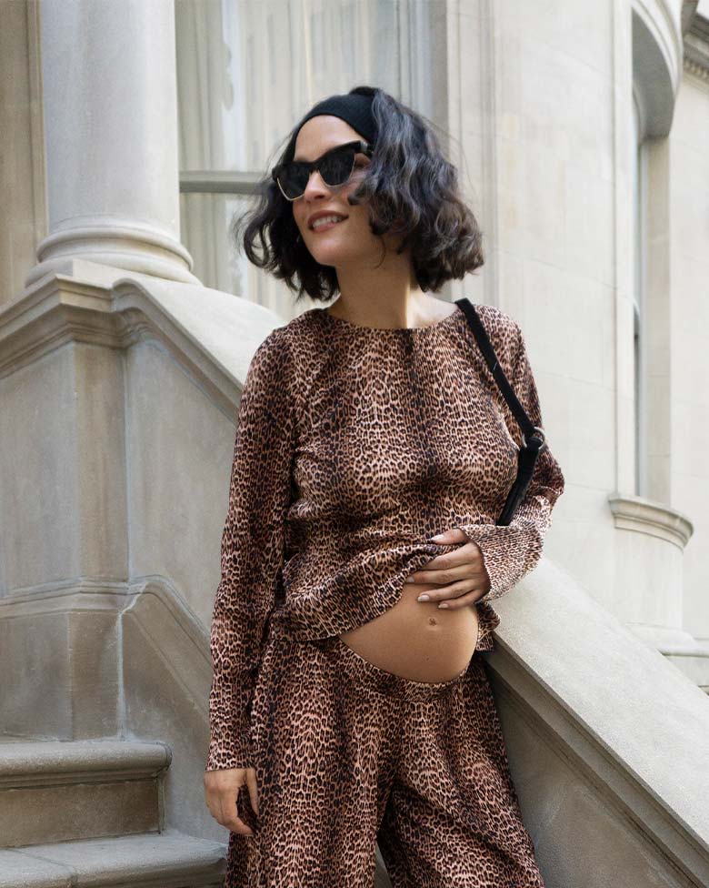 Pregnant woman poses on stone steps in an animal-print matching set.