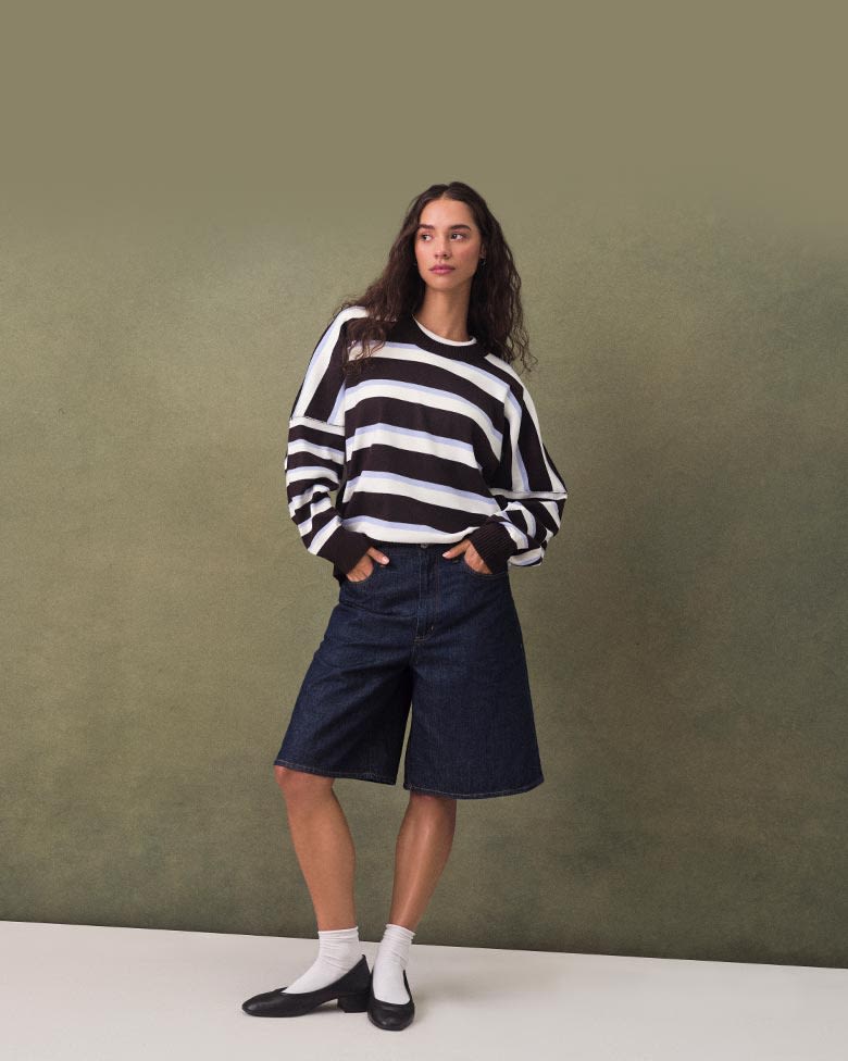 Model in large striped crew-neck and denim shorts paired with white socks and ballet flats.