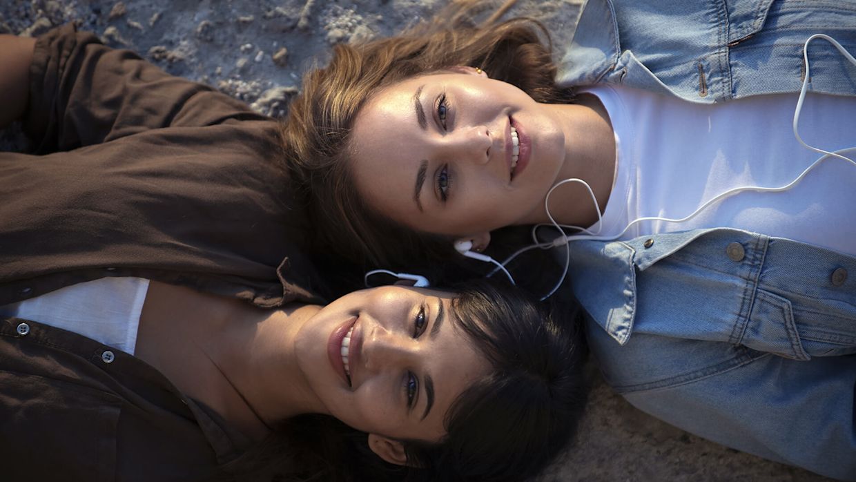 Två tjejer ligger på en strand och lyssnar på musik.