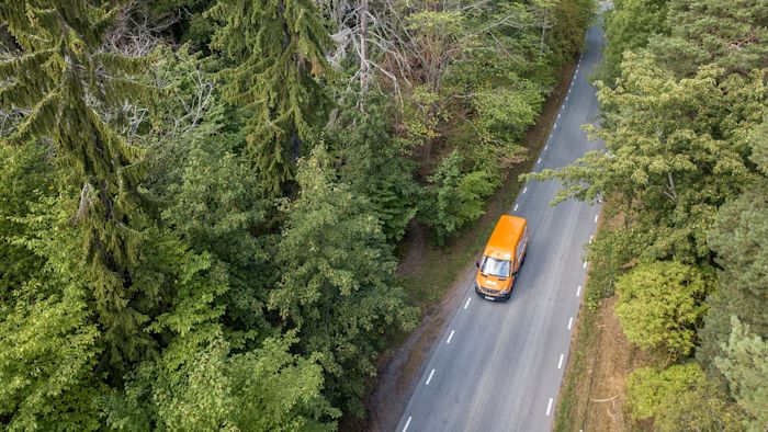 Orange lastbil kör på en väg genom skogen.
