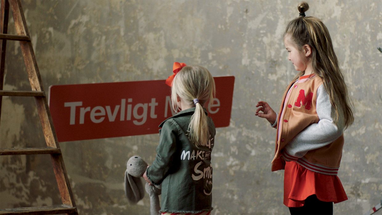 Trevligt möte - The Kids version - Två små tjejer med ryggen mot oss tittar på en röd skylt med texten Trevligt möte.