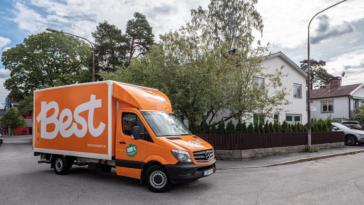 Orange bil från Best Transport i ett villaområde.