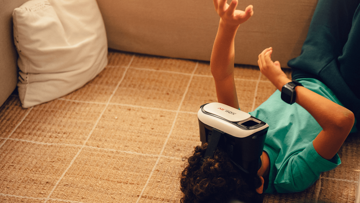 Ett barn med grön tröja ligger på golvet med VR-glasögon på sig