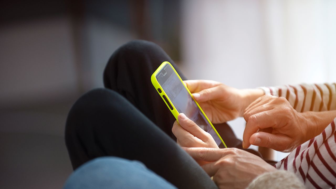 Två personer sitter tillsammmans med en mobiltelefon och går igenom något. Den ena personer håller i mobilen och den andra visar något på skärmen.