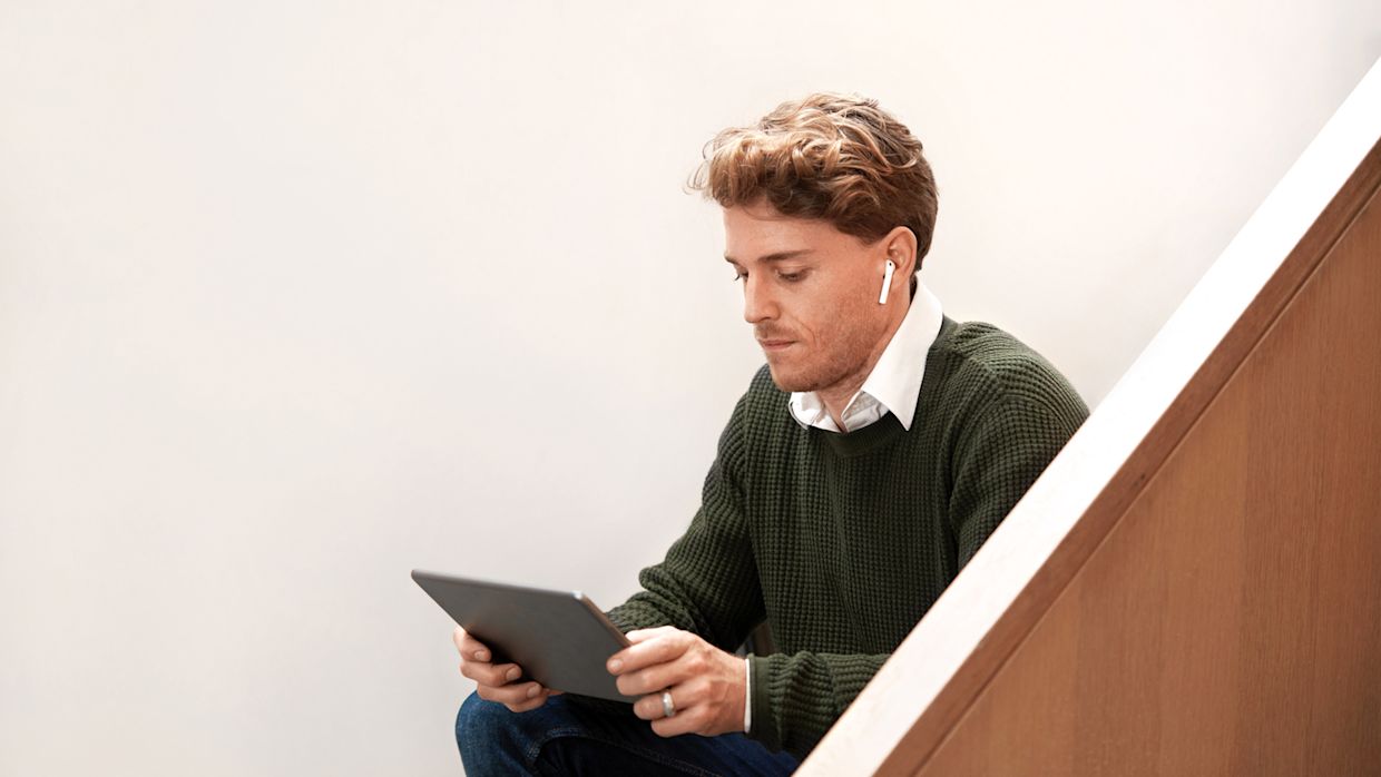 Man sittandes i trappa hållandes en surfplatta. Han har trådlösa hörlurar i öronen och ser ut att titta på någonting på surfplattan.