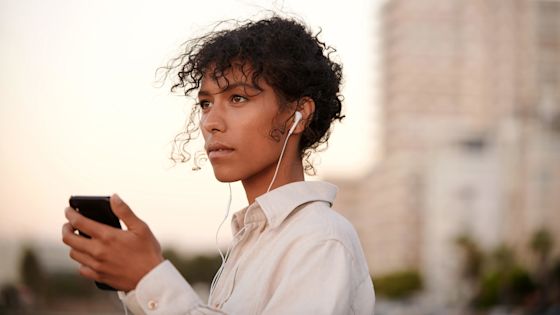 Kvinna är utomhus i statsmiljö och lyssnar på musik i i mobilen