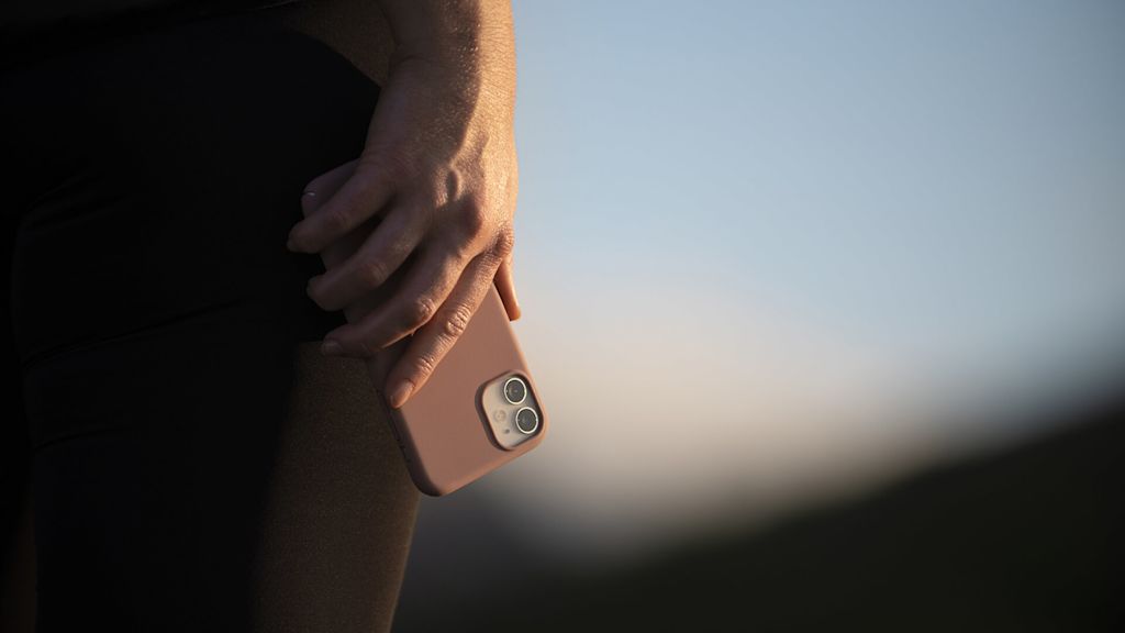 Mörk bild. Hand hållandes en mobil som pekar neråt. Mobilen har ett skal.