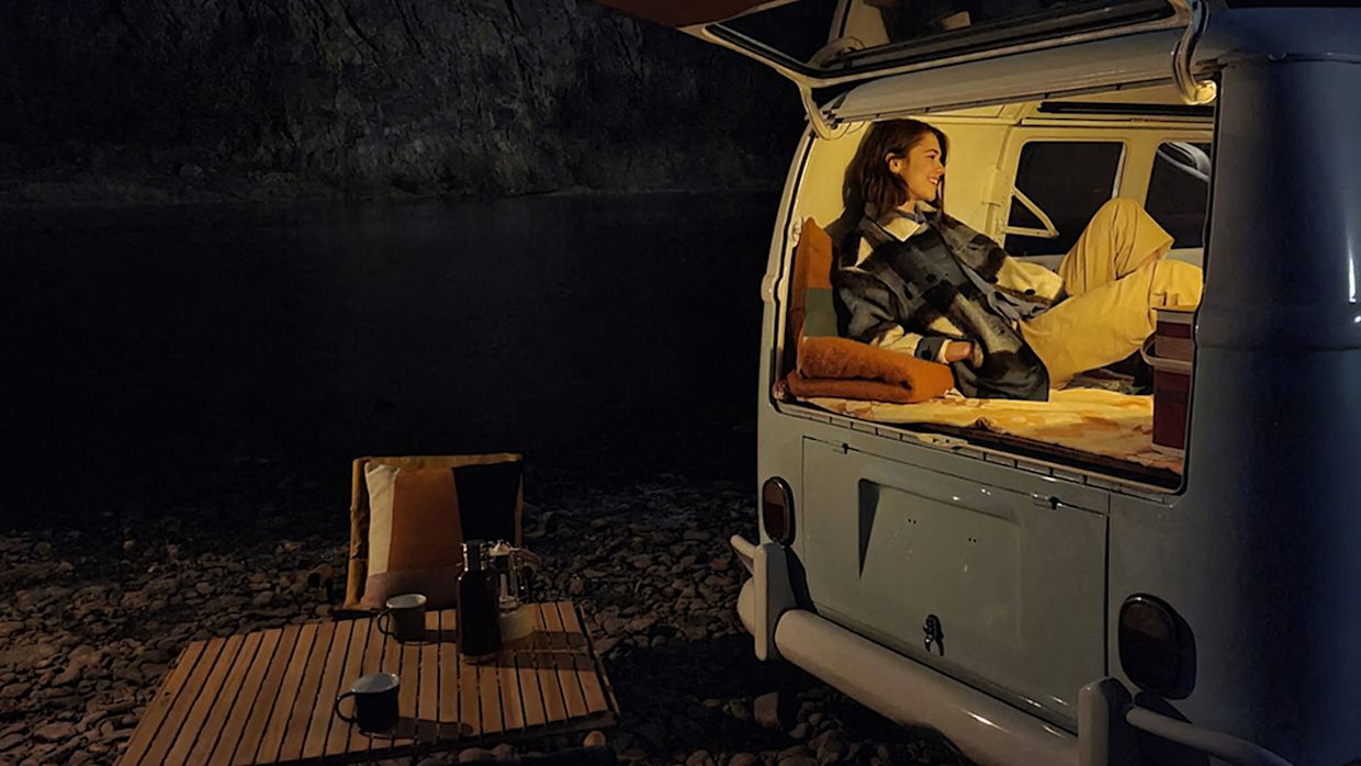 Bild som illustrerar Galaxy S21-seriens nattläge. Ljus förgrund, kvinna i skåpbil. Mörk bakgrund, campingplats.