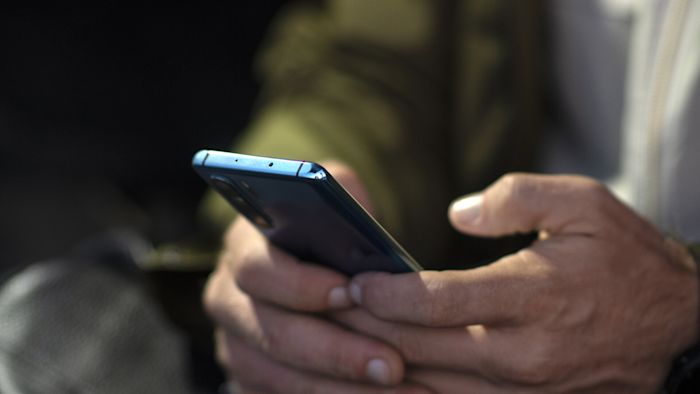 Person med mobil i båda händerna. Mobilen och händerna i förgrunden, personen, något suddig, i bakgrunden.