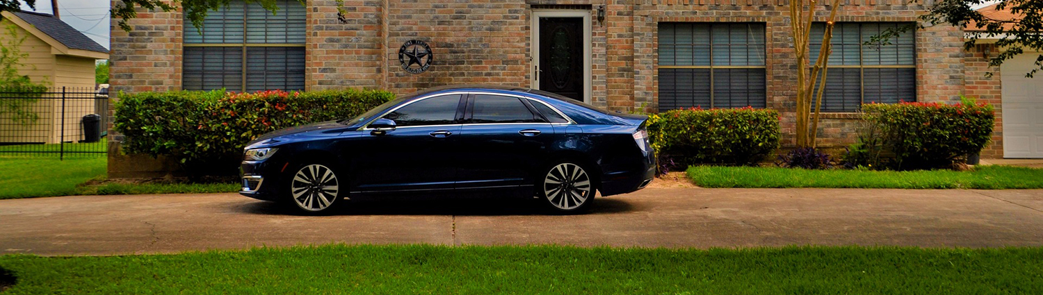 A blue car parked in a driveway in front of a brick house..