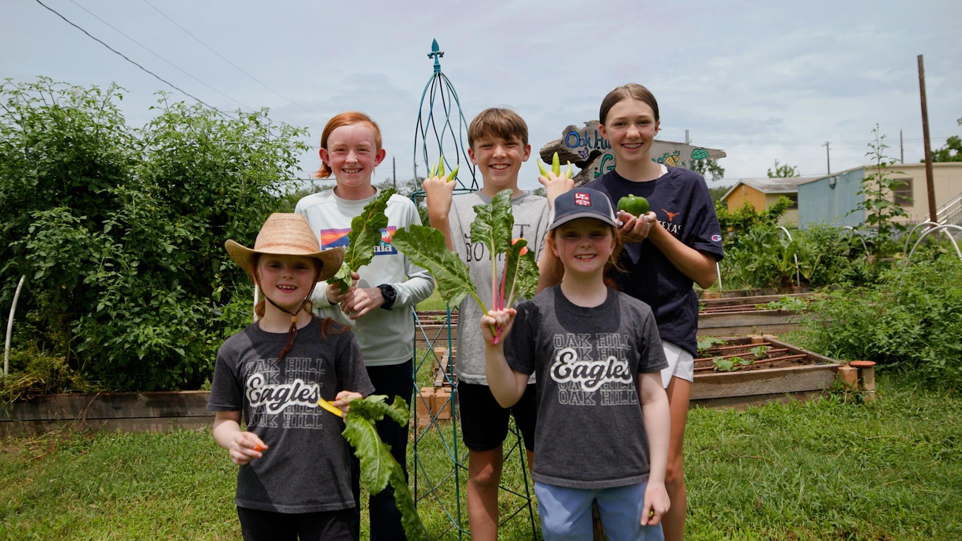 A group of children pose with vegetables picked from a community garden