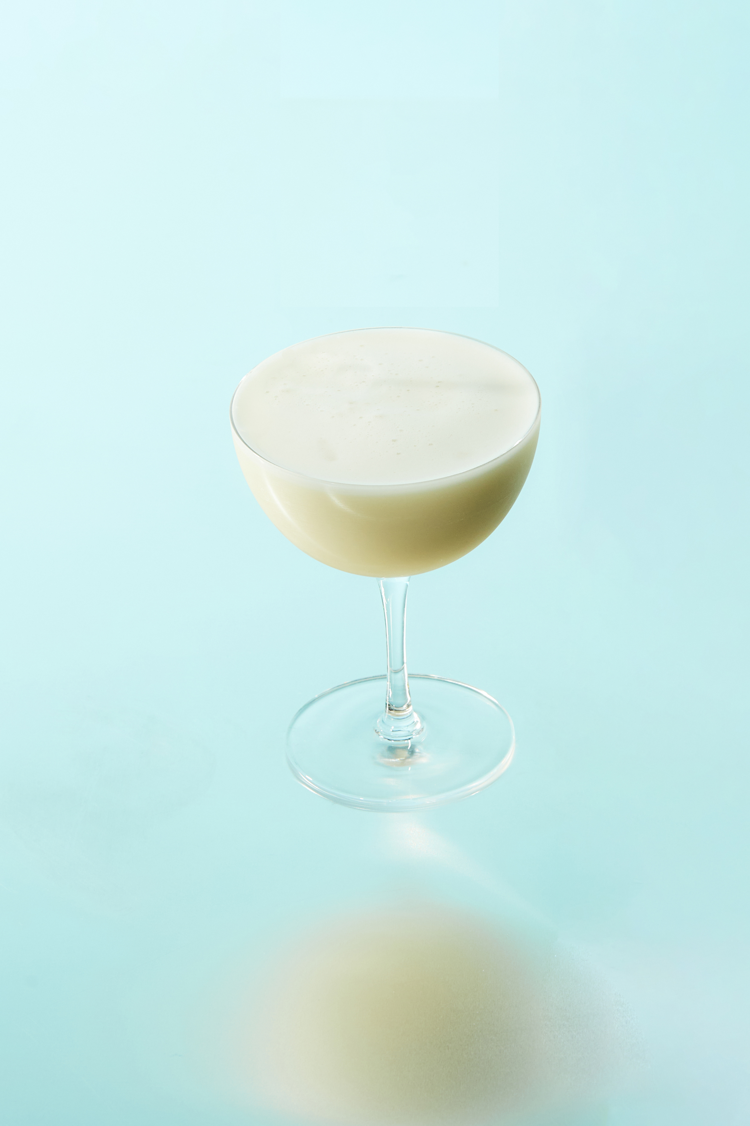 A frothy The Singleton Rhubarb Sour cocktail served in a coupe glass on a light blue background, showcasing the signature Singleton cocktail recipe
