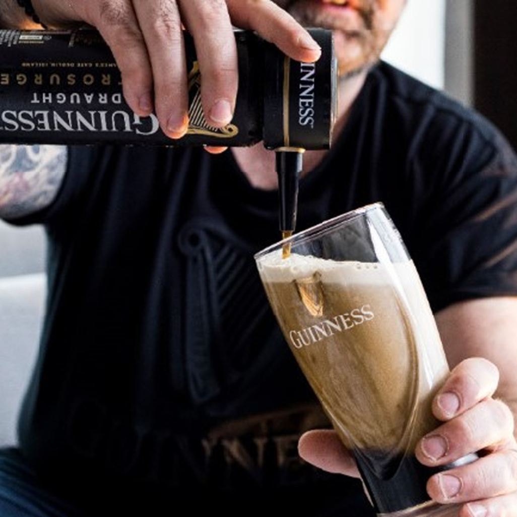 Person pouring Guinness Draught from a can into a branded pint glass at home