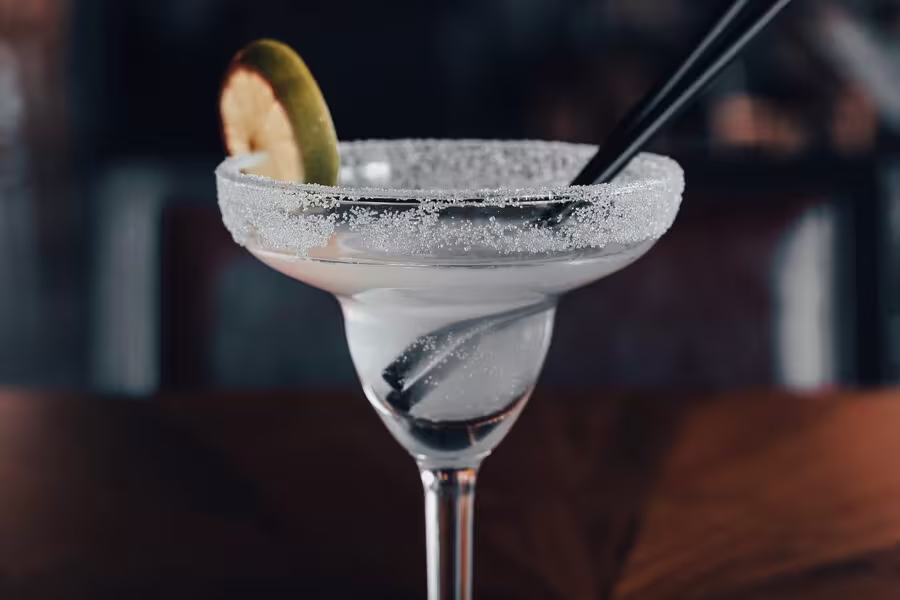 A margarita cocktail in a salt-rimmed glass, garnished with a lime slice and served with two black straws.