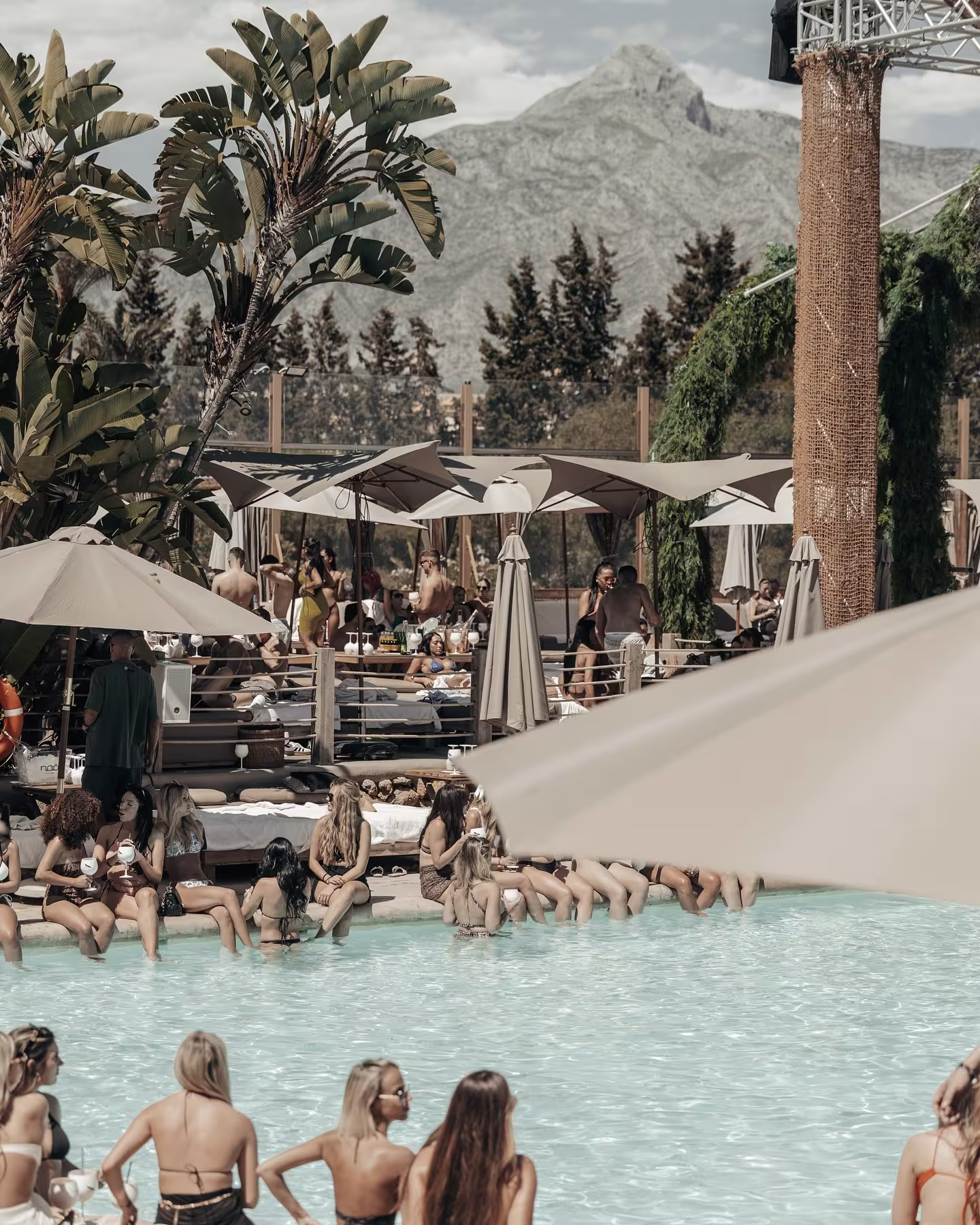 Pool party en Nao Pool Club, Marbella, con vistas a la montaña, sombrillas elegantes y ambiente exclusivo junto a la piscina.