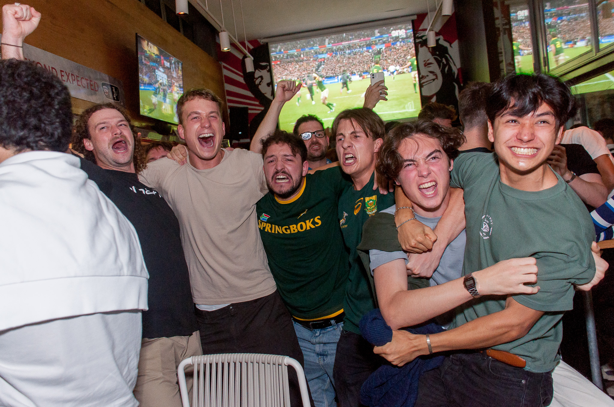La imagen muestra un grupo de personas en el interior de Belushi´s Bar. Disfrutando un evento deportivo en directo en las múltiples pantallas.