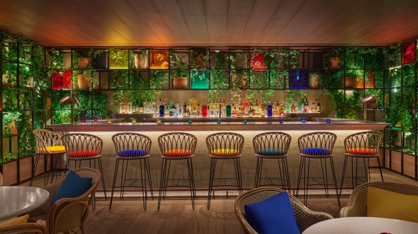 Oroya Madrid, un bar vibrante con taburetes coloridos, vegetación decorativa y una barra iluminada, perfecto para disfrutar de cócteles únicos.