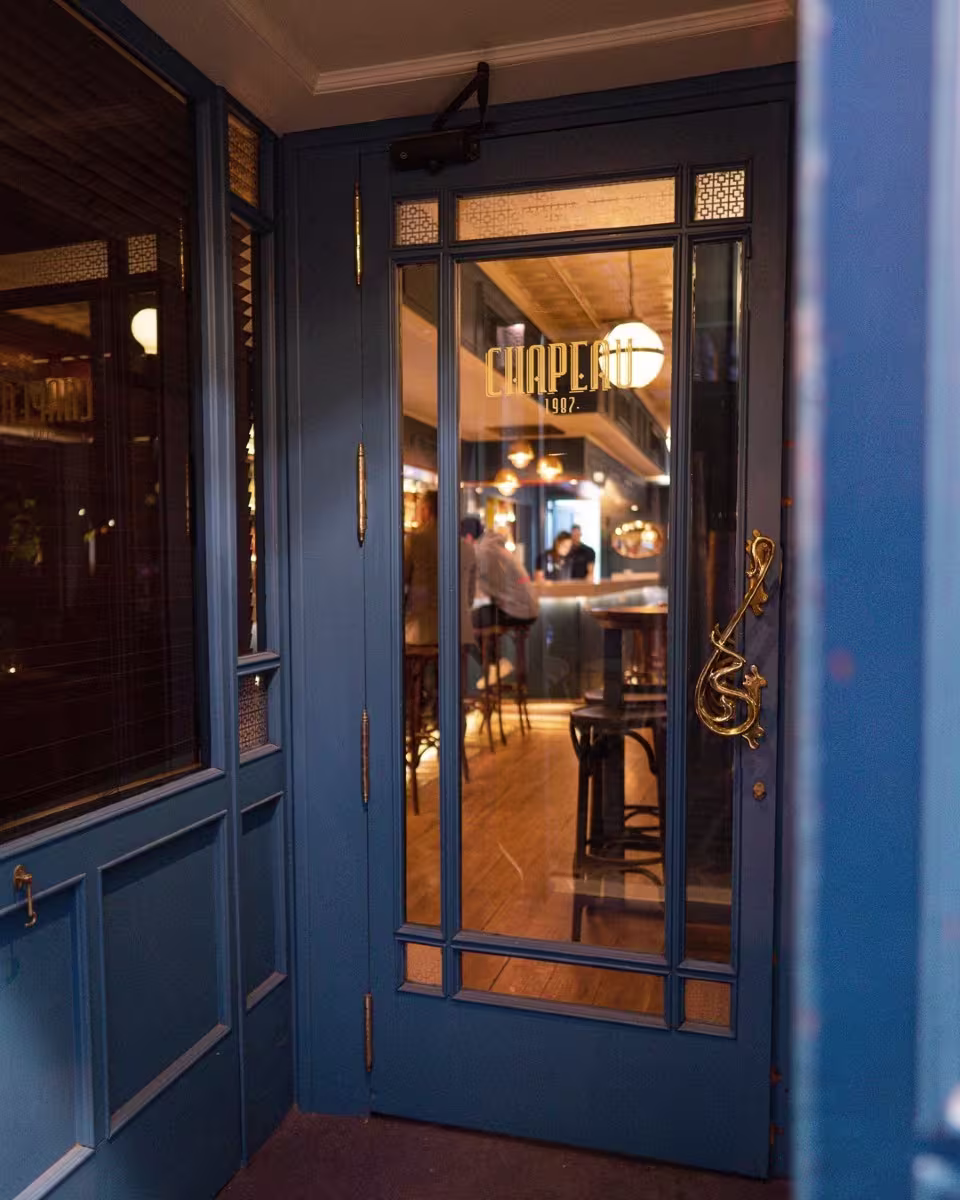 Entrada del restaurante Chapeau 1987, con una puerta azul y detalles dorados que reflejan su ambiente acogedor y elegante.
