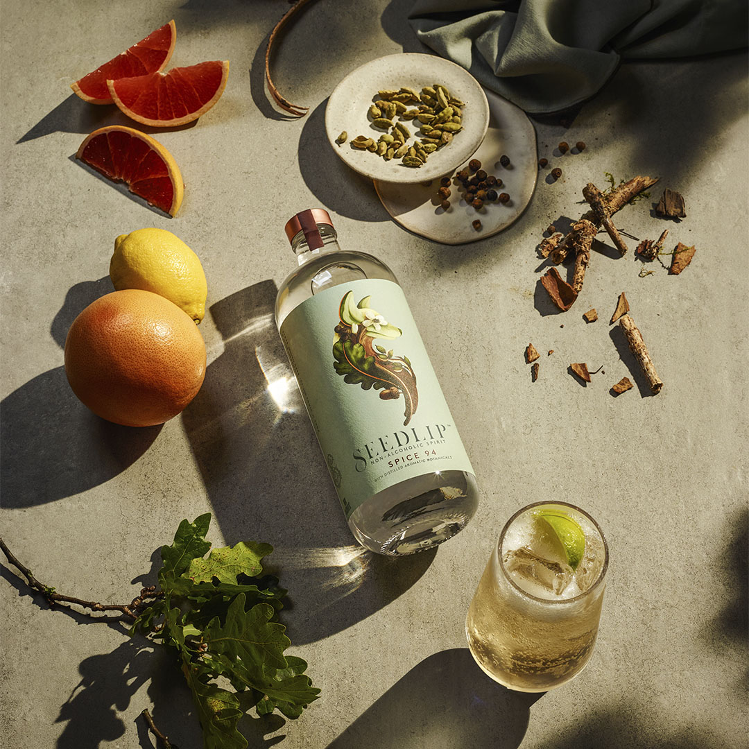 Seedlip Garden 108 bottle surrounded by fresh grapefruit, lemon, herbs, and spices on a sunlit surface