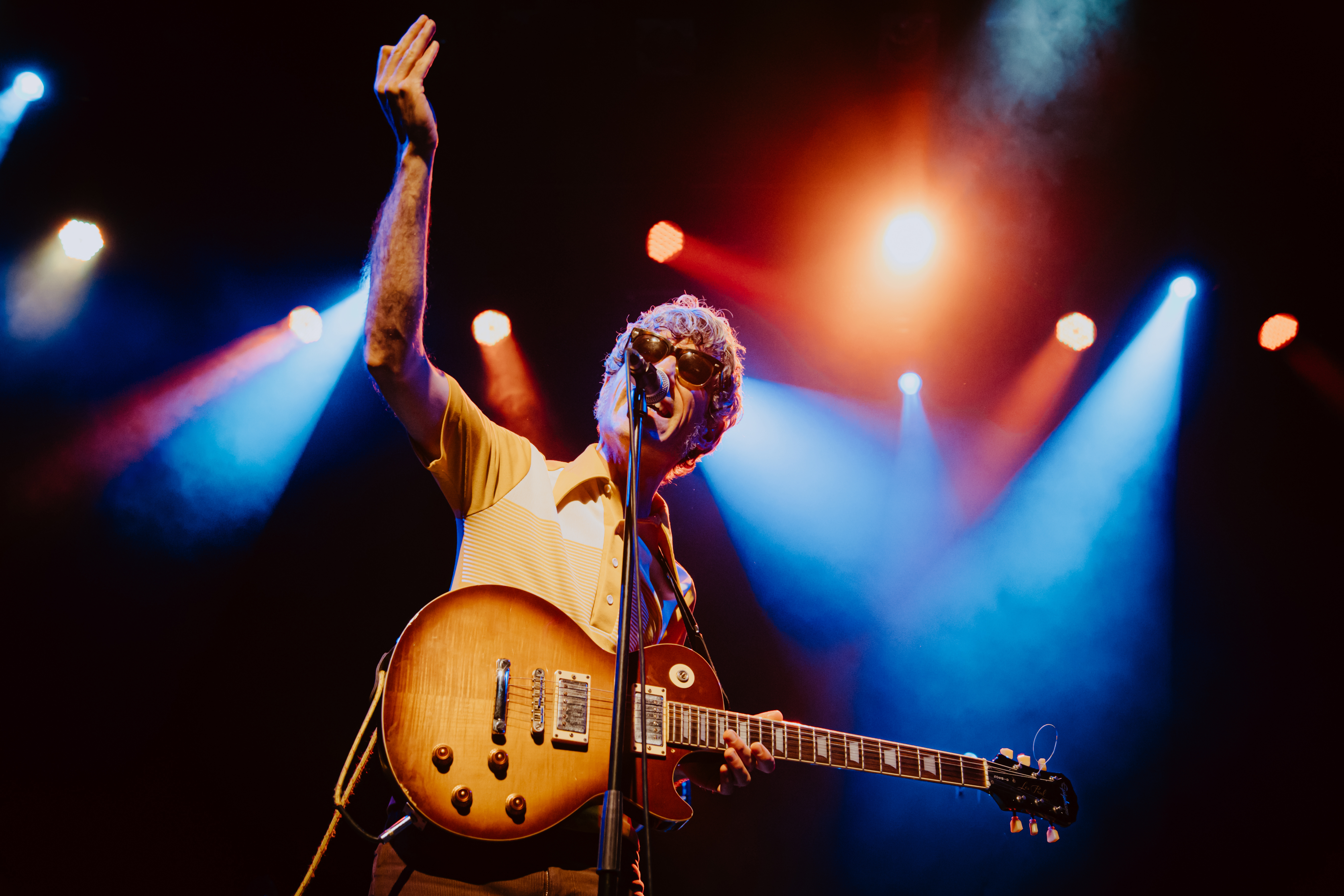 The Bar | Paral.lel 62 - Primer plano de un cantante con guitarra eléctrica en el escenario, bajo luces de colores durante una actuación en vivo.