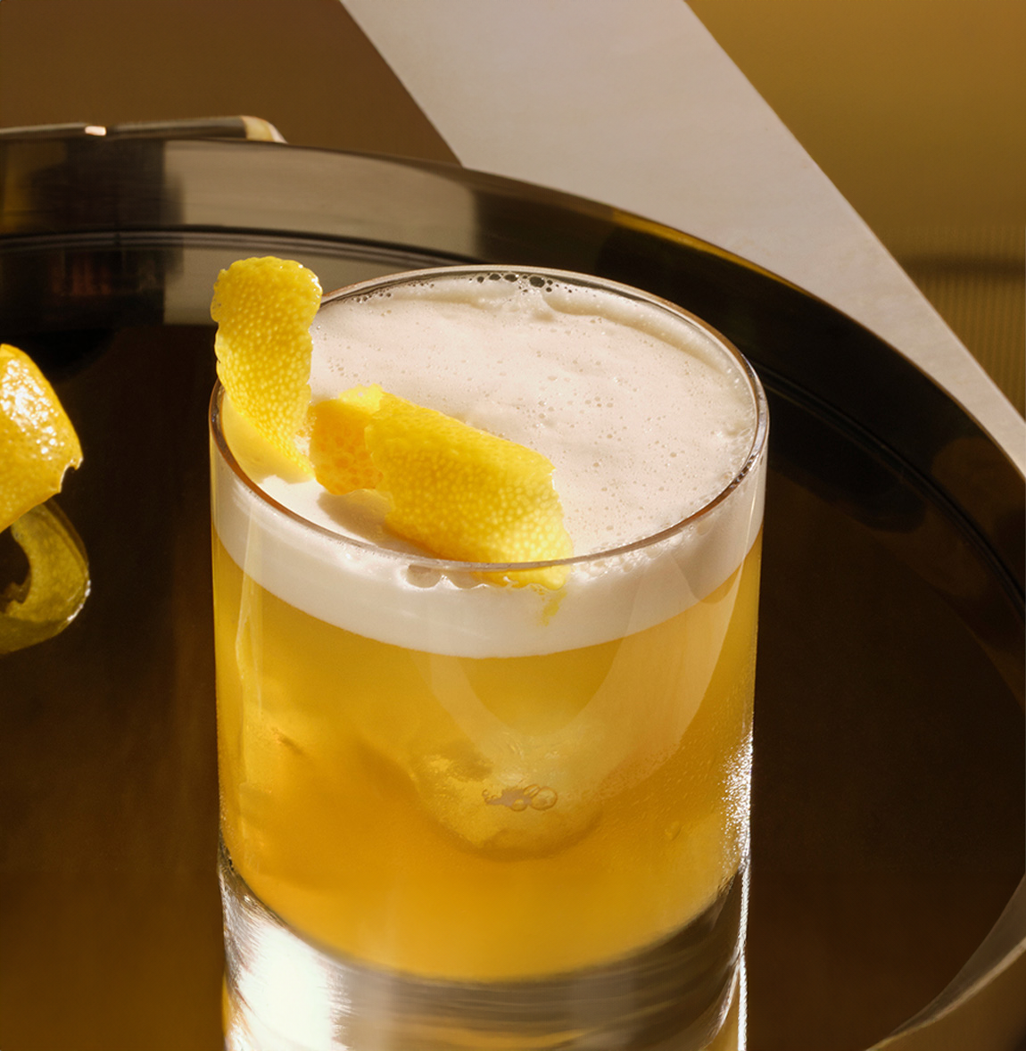 Bulleit whiskey sour cocktail garnished with a lemon twist on a reflective tray