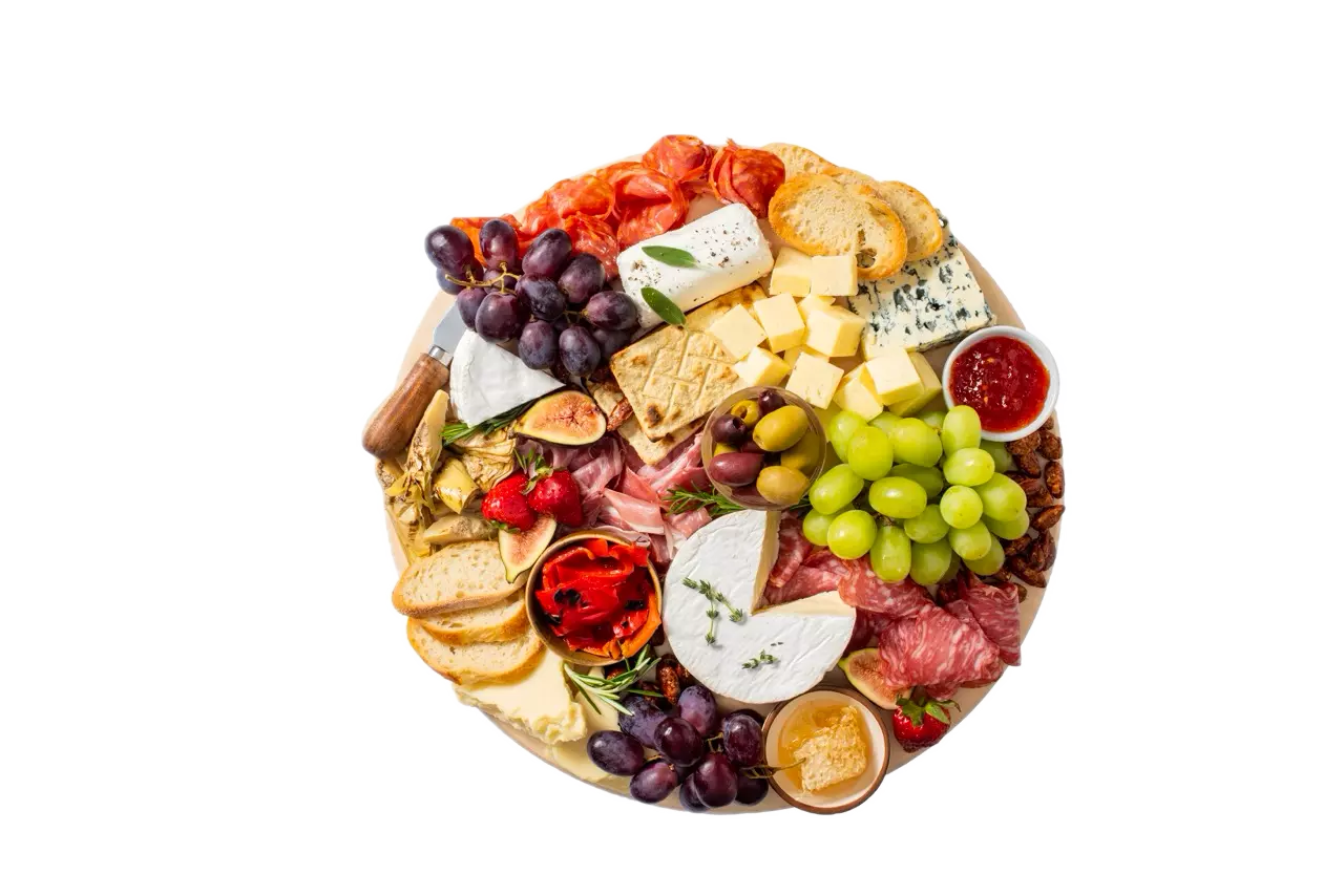 A round charcuterie board with assorted cheeses, cured meats, crackers, grapes, strawberries, jam, nuts, and red pepper slices arranged neatly.