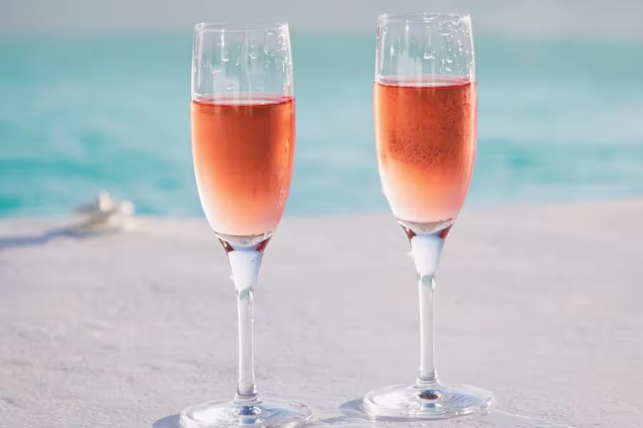 Two glasses of rosé wine on a white surface with a blurred blue water background.