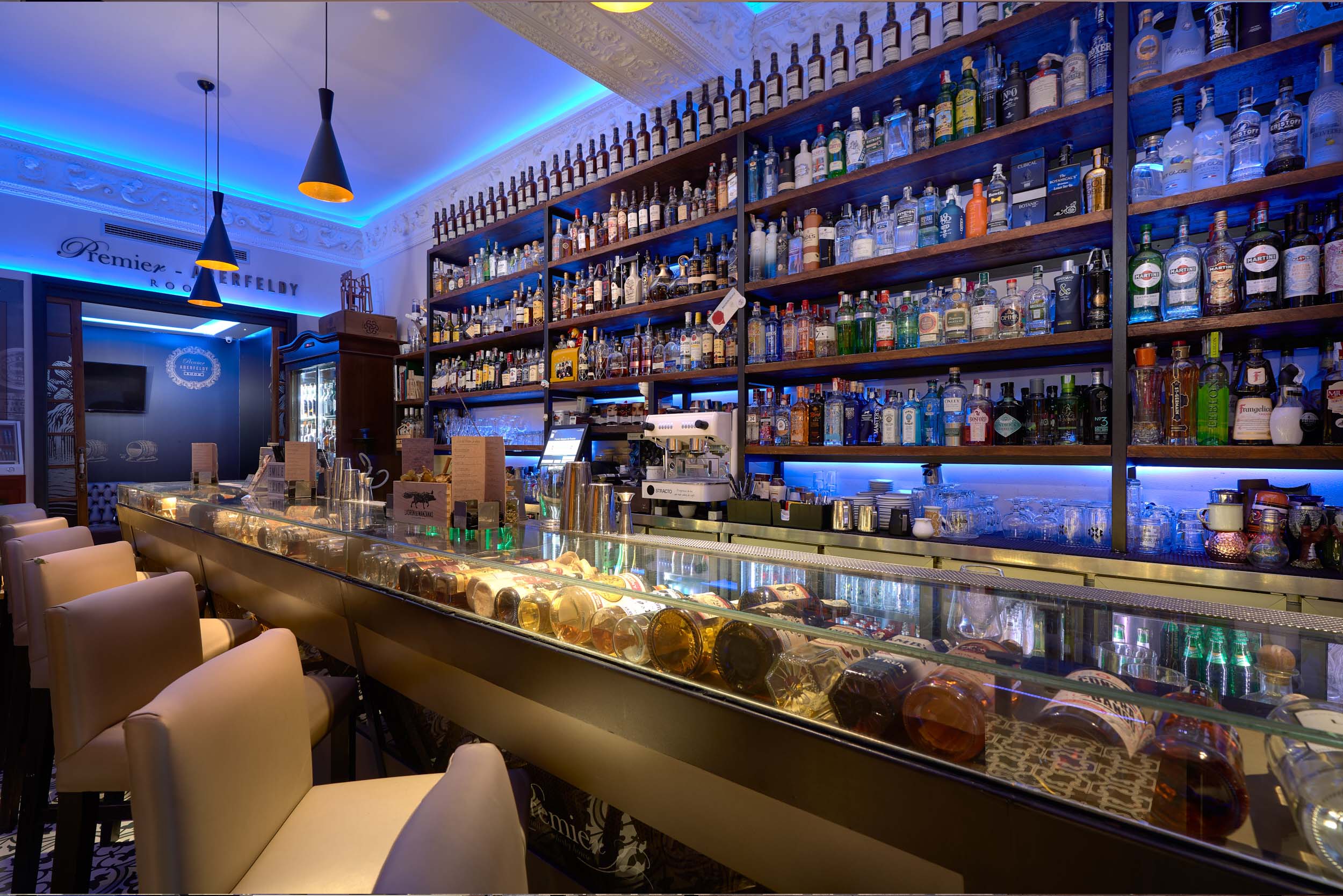 Interior de Premier Cocktail Gin & Rum Selections con iluminación azul, cómodos sofás y un ambiente moderno y sofisticado.