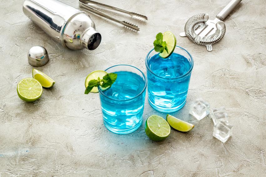 Blue lagoon cocktail sitting on a weaved mat in a beach setting