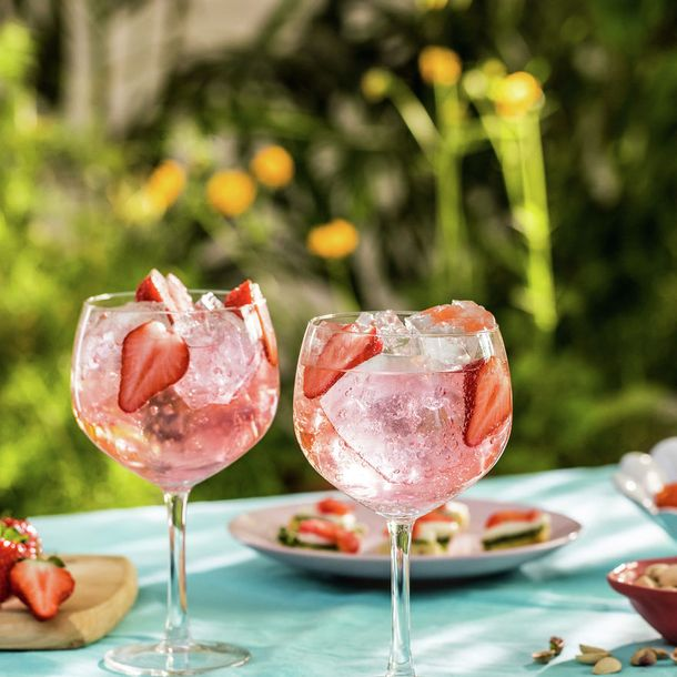 Gordon's pink gin and tonic cocktails with ice and fresh strawberry slices served outdoors on a sunny day