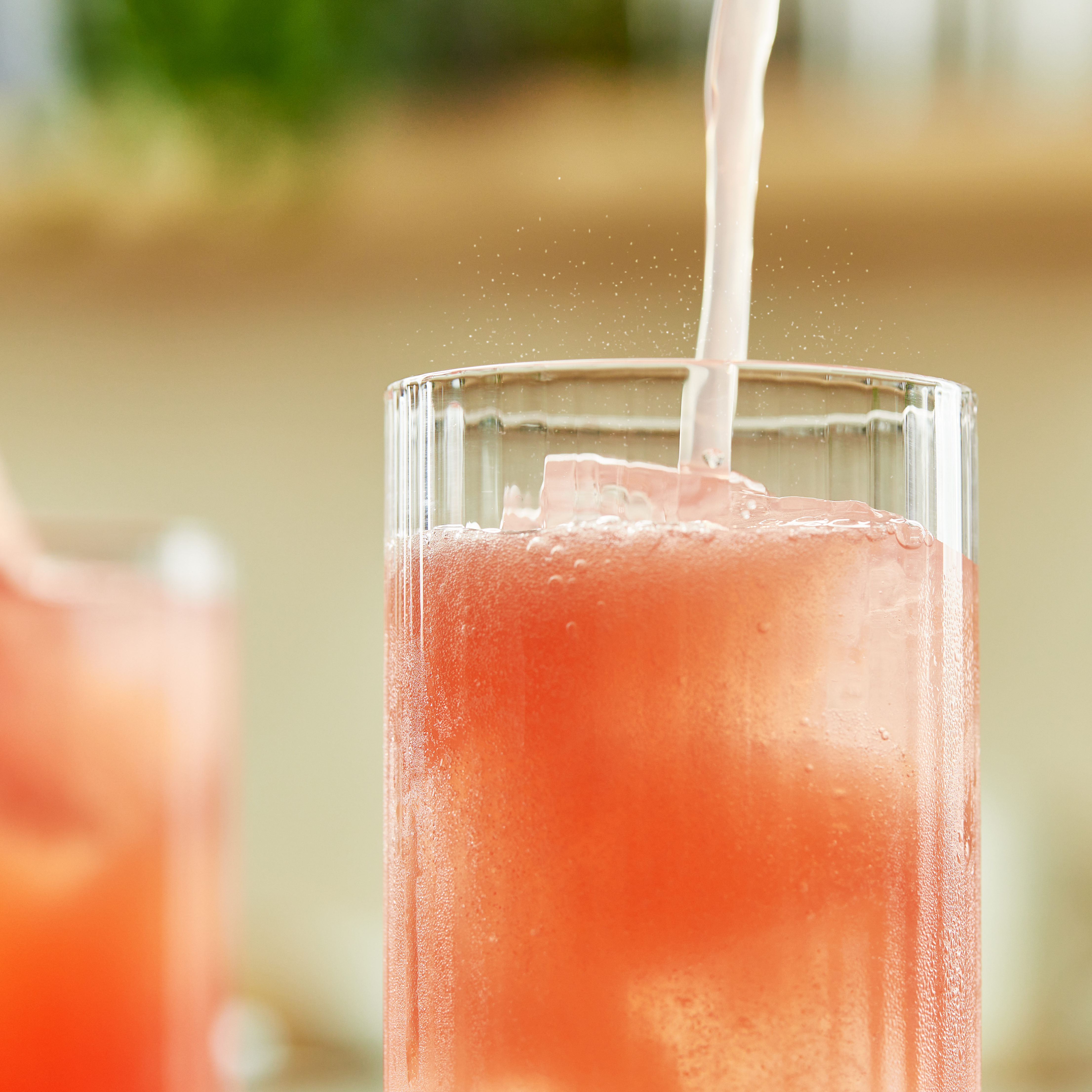 A close up of pink fizzy liquid being poured into a Collins glass