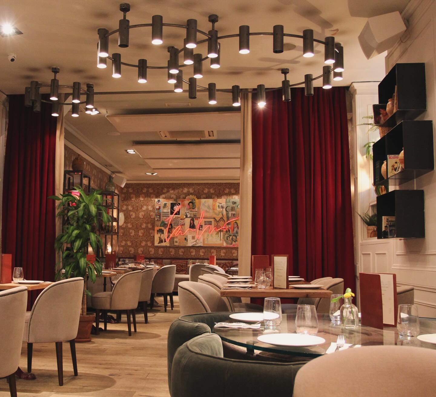 Interior de Makkila, con cortinas rojas, mesas elegantes, sillas tapizadas, iluminación moderna y una decoración acogedora con detalles artísticos.