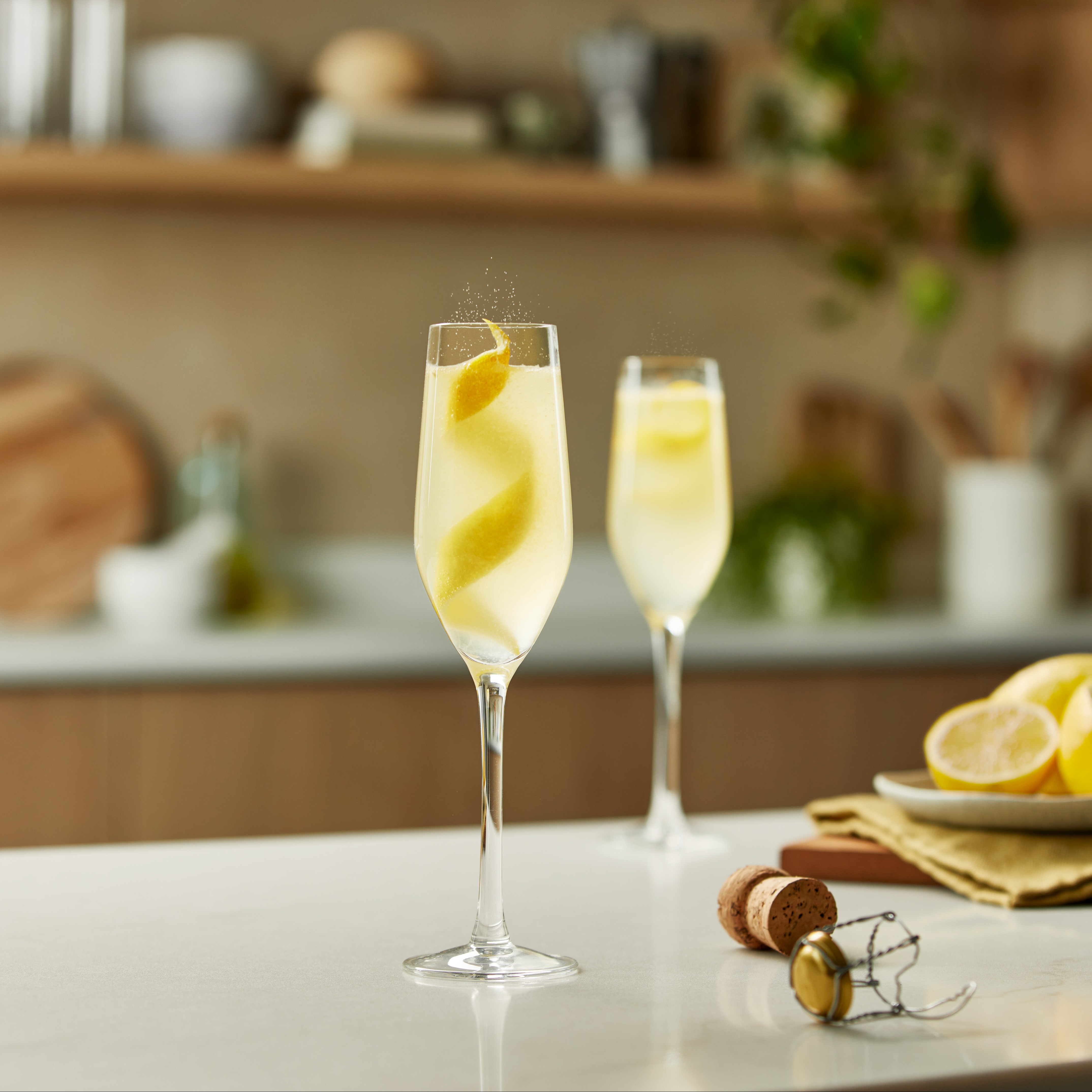 Two French 75 cocktails on a kitchen counter with lemon twist garnishes