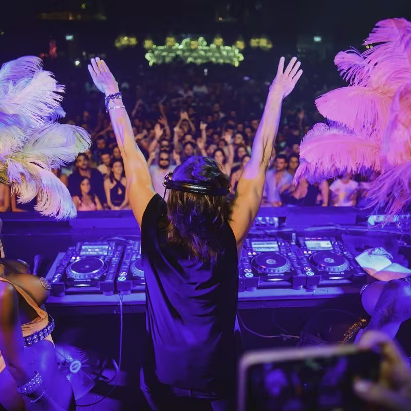 El DJ en BCM electriza la multitud bajo luces vibrantes y plumas, creando una noche inolvidable en Magaluf.