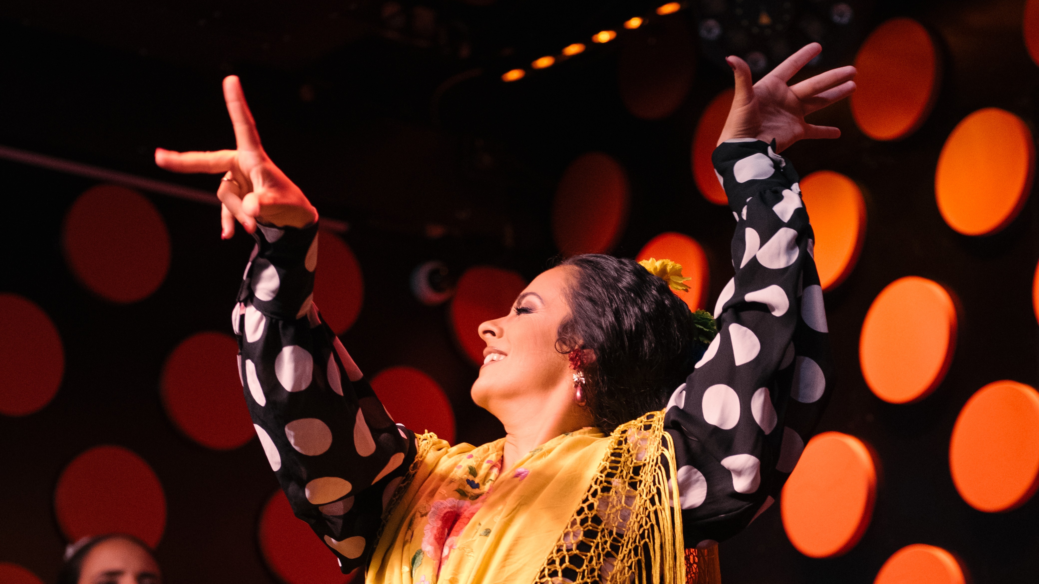 La imagen muestra a una bailaora flamenca con un traje flamenco de lunares, en el escenario del tablao Tarantos.