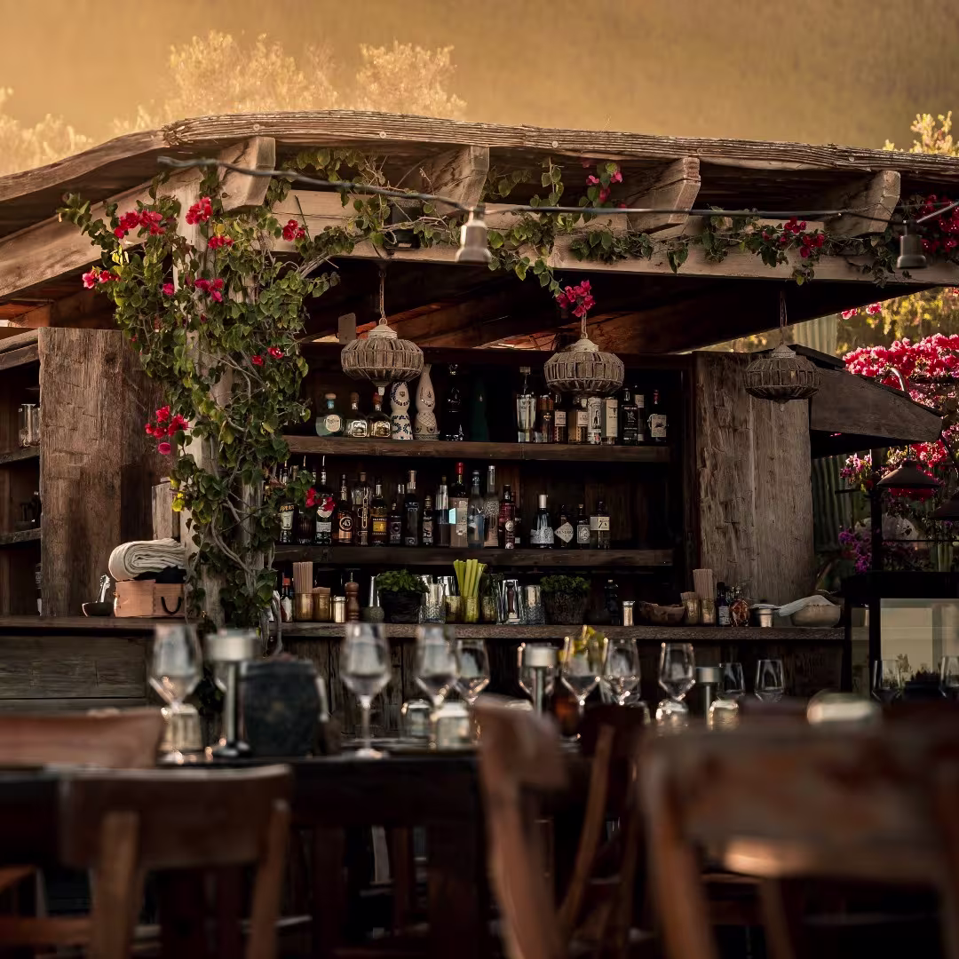 Bar al aire libre de Casa Maca, con una estructura rústica de madera adornada con flores, iluminación cálida y una atmósfera encantadora.