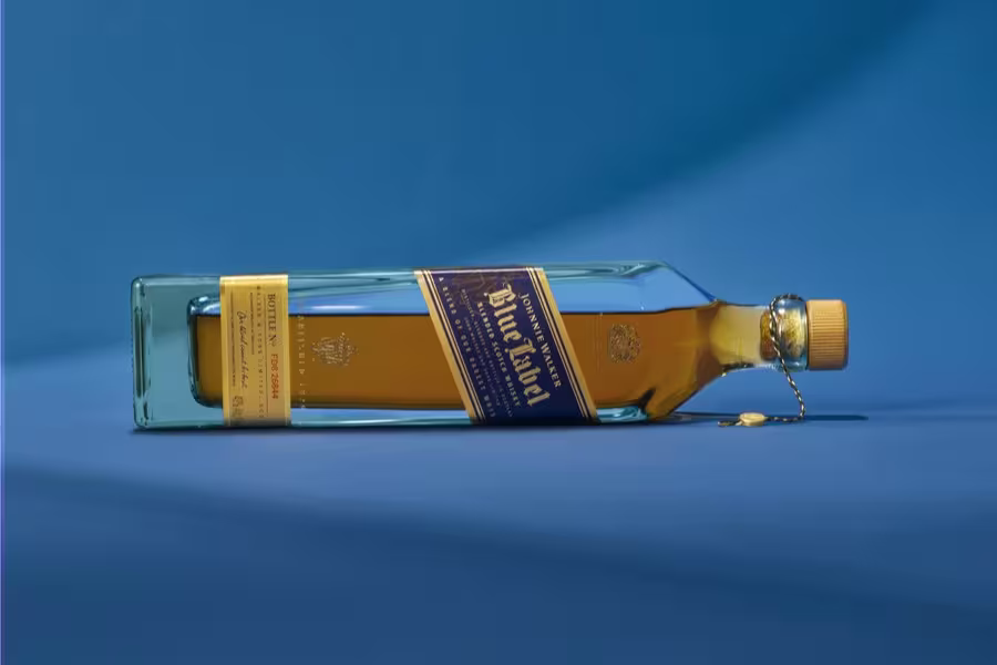 A rectangular bottle of amber-colored whiskey with a blue and gold label is lying on its side against a blue background.