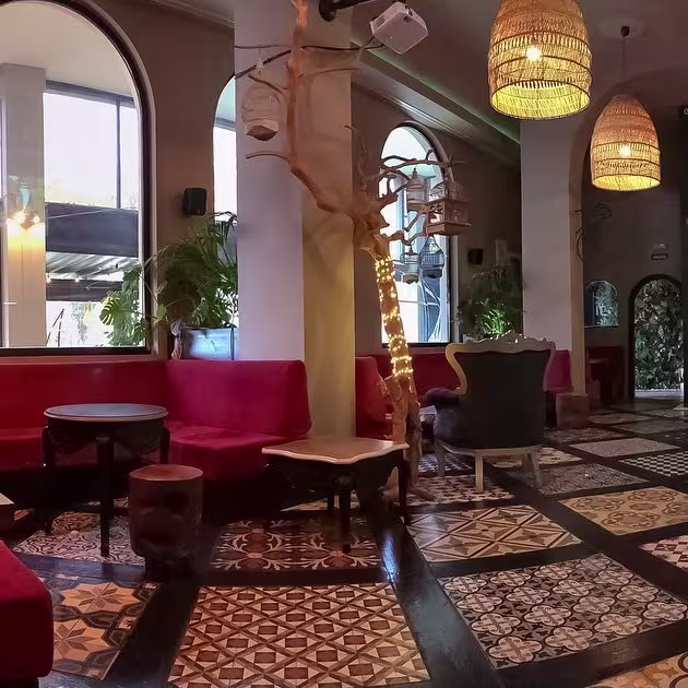 Bohra Shisha Cocktail destaca por su suelo decorativo, sofás rojos y detalles elegantes como lámparas tejidas y árboles iluminados.