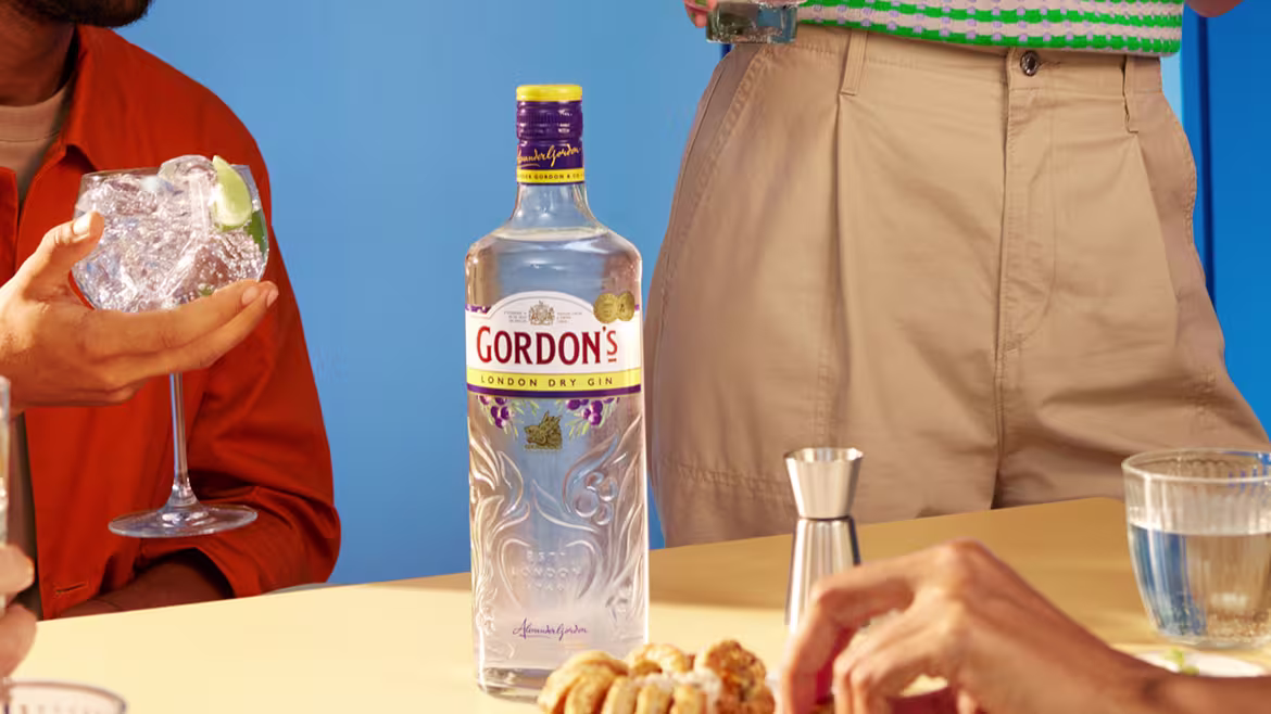 People enjoying Gordon's London Dry Gin cocktails with lime at a table with snacks in a bright blue room