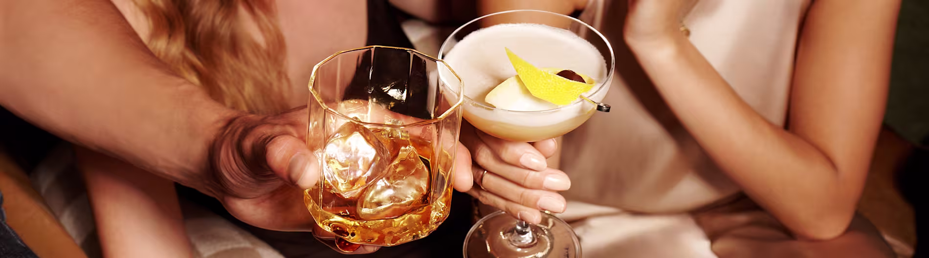 Közelkép két kézről, akik prémium whiskyt és savanyú koktélokat tartanak egy meghitt környezetben