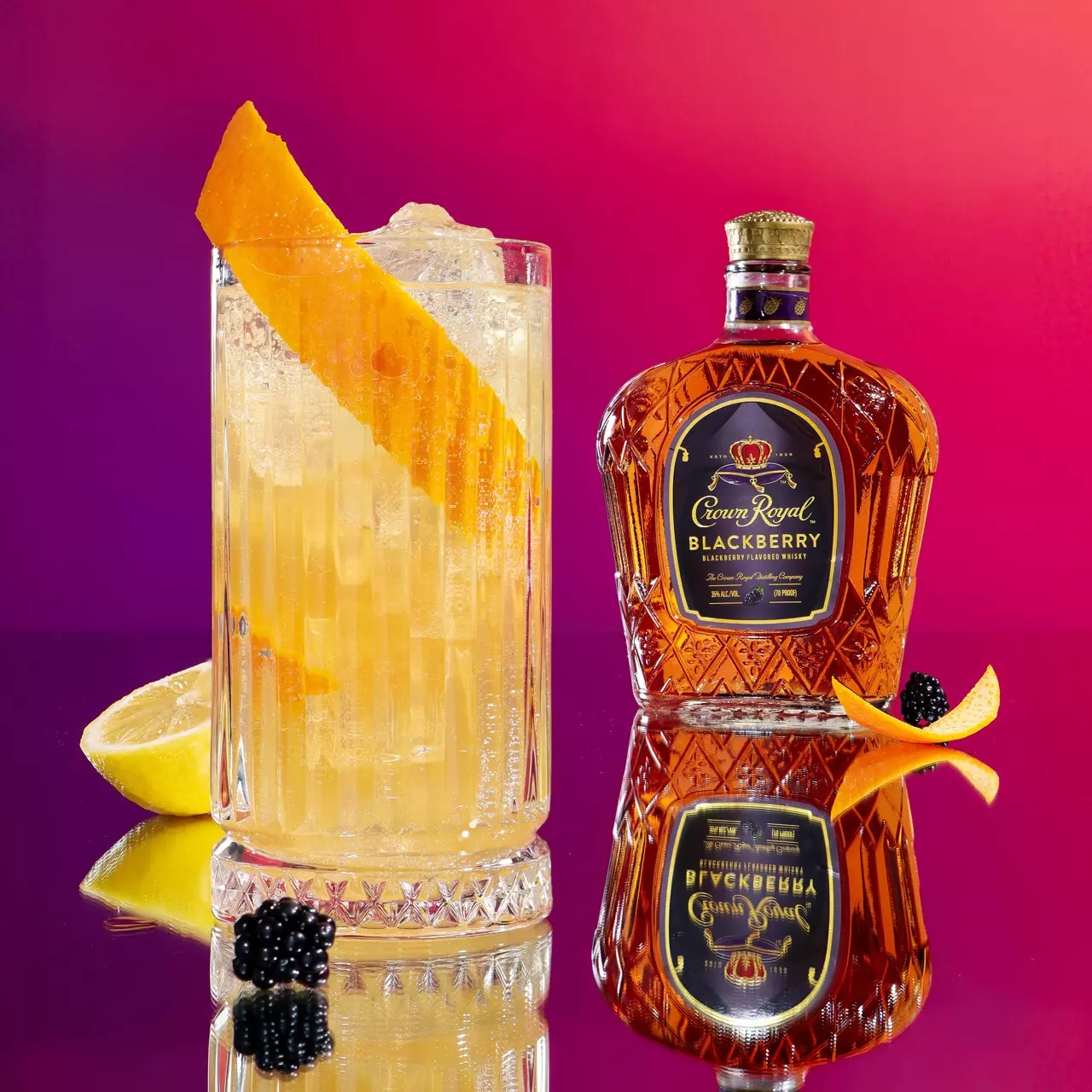A glass of cocktail garnished with an orange peel sits next to a bottle of Crown Royal Blackberry whisky, with a blackberry and orange peel placed nearby against a pink gradient background.