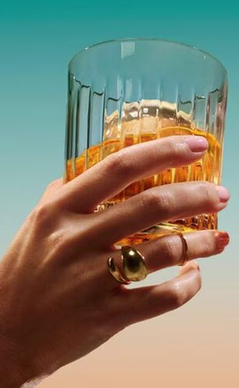 A close-up of a hand holding a crystal glass of The Singleton single malt Scotch whisky, showing the whisky's warm amber colour