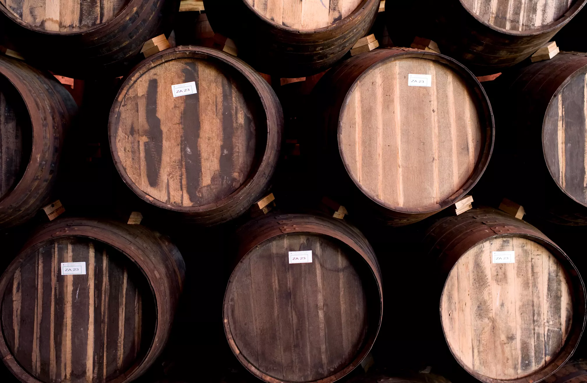 A group of wooden barrels stacked horizontally, each with a small white label on the top surface.