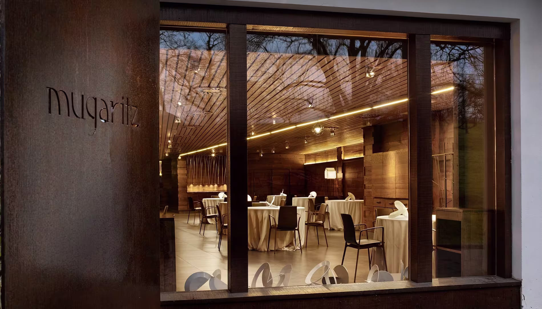 Entrada y vista interior del restaurante Mugaritz, destacando su diseño elegante y moderno con mesas dispuestas para el servicio.