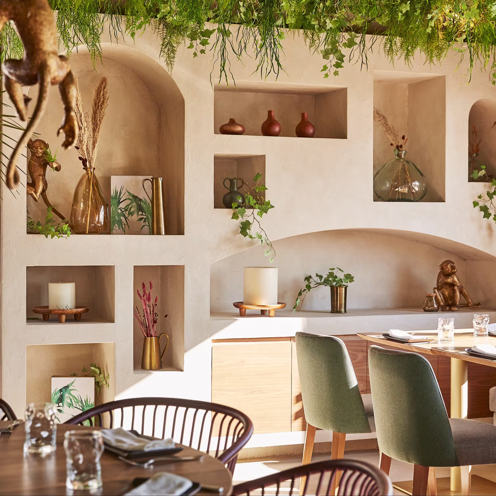 La imagen muestra un espacio interior de El Jardin de DIana, con un diseño moderno y natural. Las paredes están adornadas con estanterías empotradas que exhiben varios objetos decorativos como jarrones, esculturas y plantas.