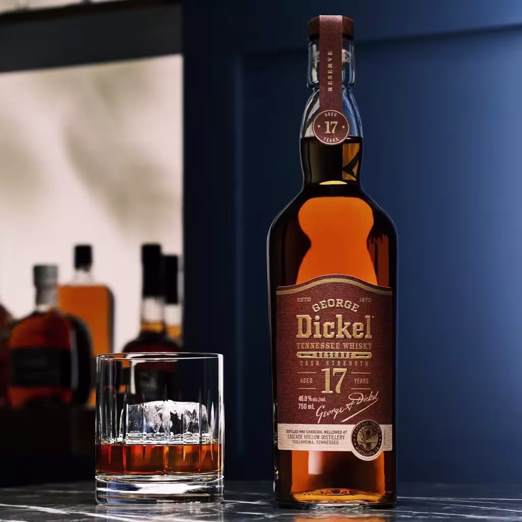 A bottle of George Dickel 17-year-old Tennessee whisky stands next to a glass of whisky on a dark countertop, with more bottles blurred in the background.