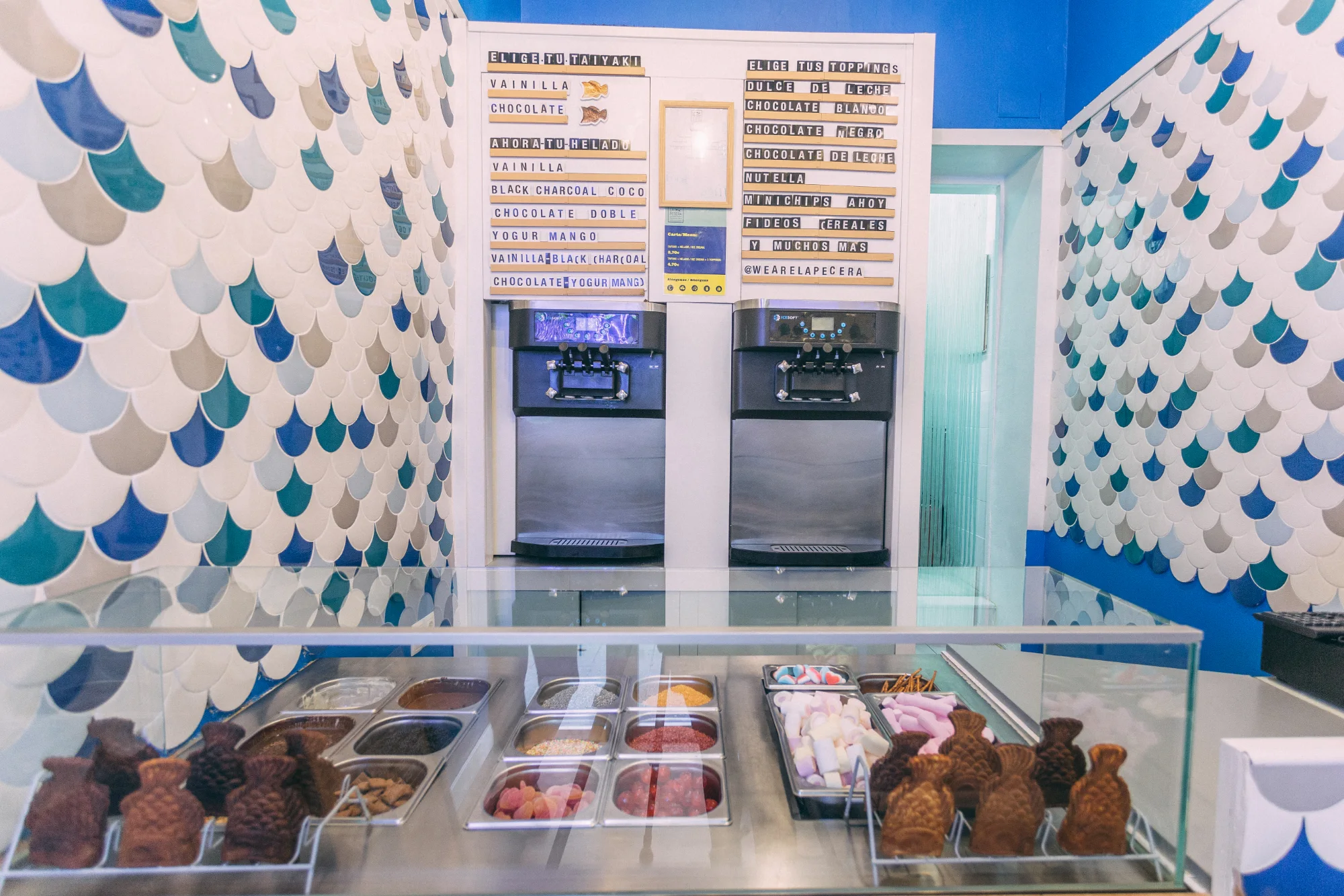 Interior de La Pecera Velarde con paredes de escamas marinas, vitrinas con toppings y taiyakis listos para rellenar.