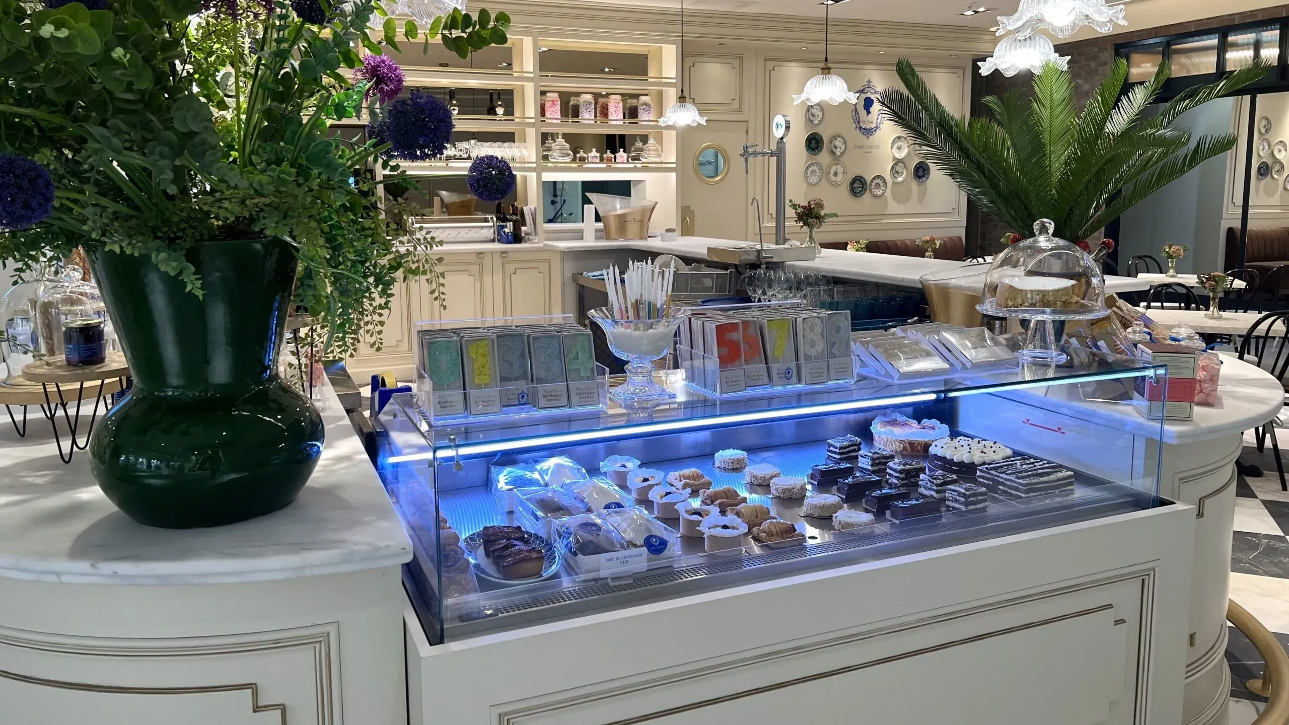Mostrador de pastelería en un entorno elegante y luminoso, con tartas, dulces y decoración clásica de inspiración francesa.
