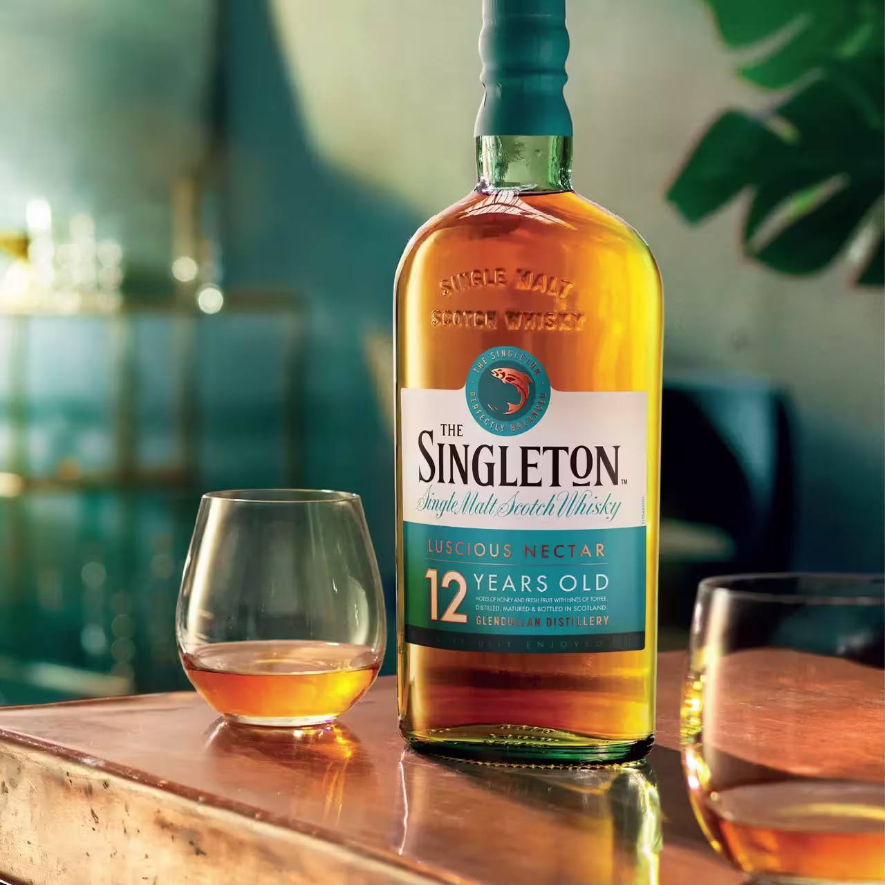 A bottle of The Singleton 12 Years Old single malt scotch whisky stands on a table next to two glasses with whisky.