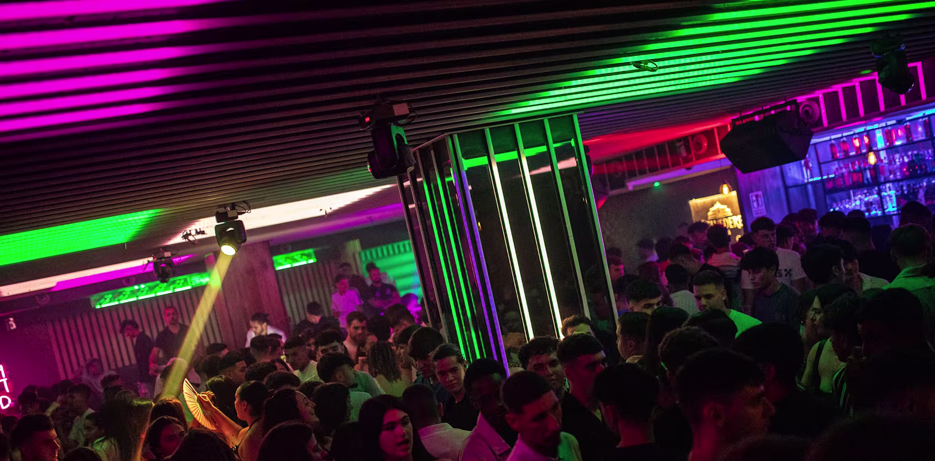 Pista de baile llena en Coltan y Benavente con luces verdes y púrpuras. Ambiente vibrante y multitud disfrutando de la noche.